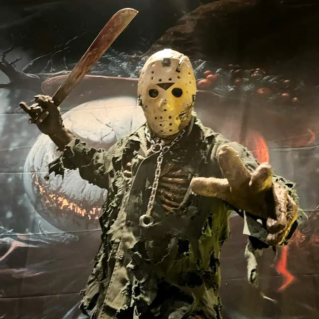 Ator fantasiado de criatura de terror recepcionando convidados na entrada de um evento corporativo temático.