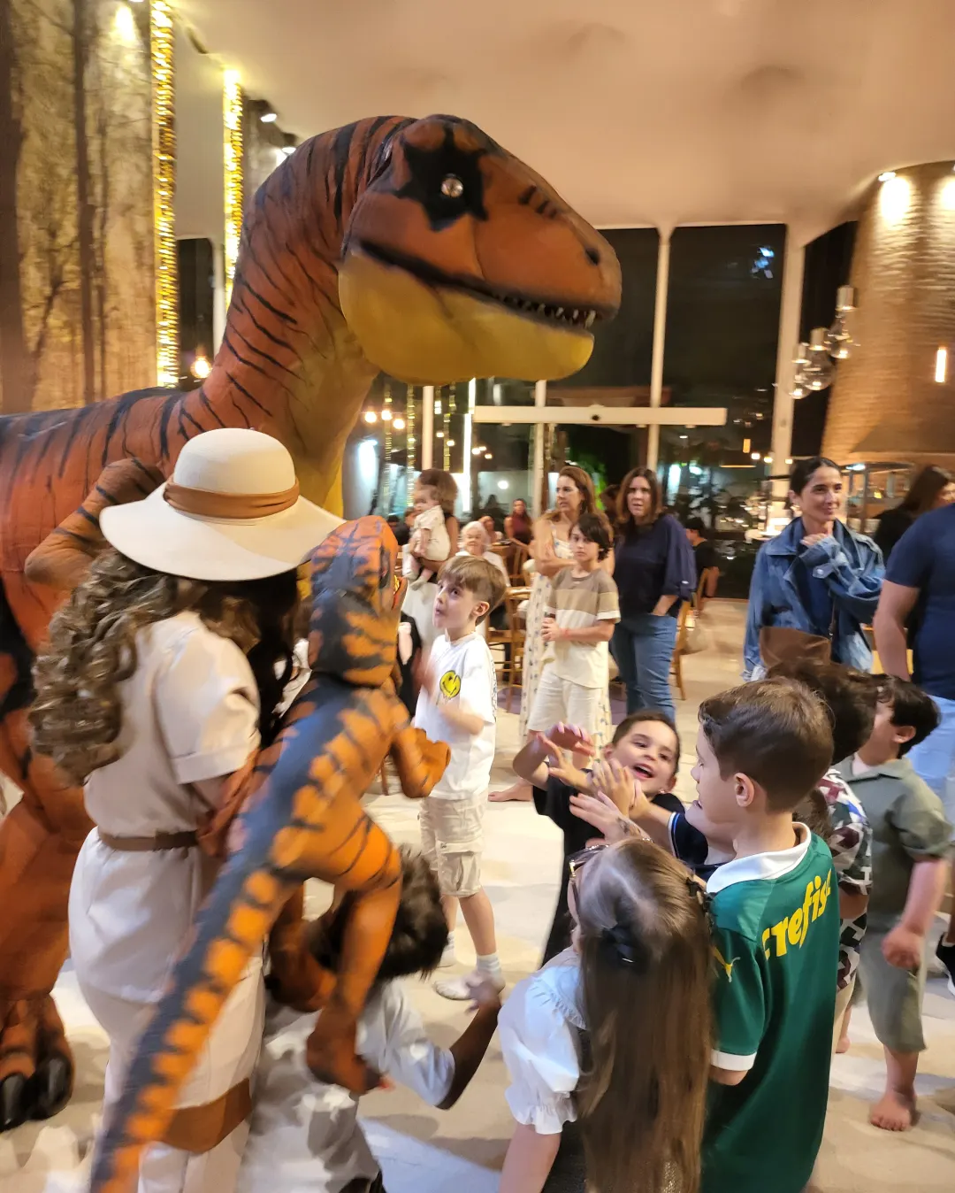 Convidados posando ao lado do ágil Velociraptor Laranja Personagem Vivo em São Paulo