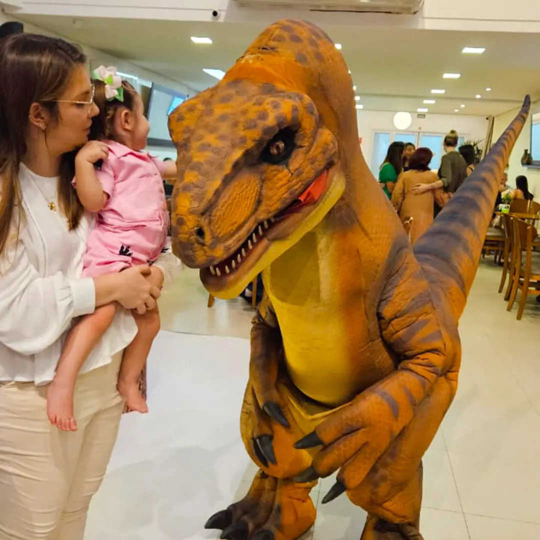 Crianças sorrindo e interagindo de forma segura com dinossauro laranja em buffet infantil.