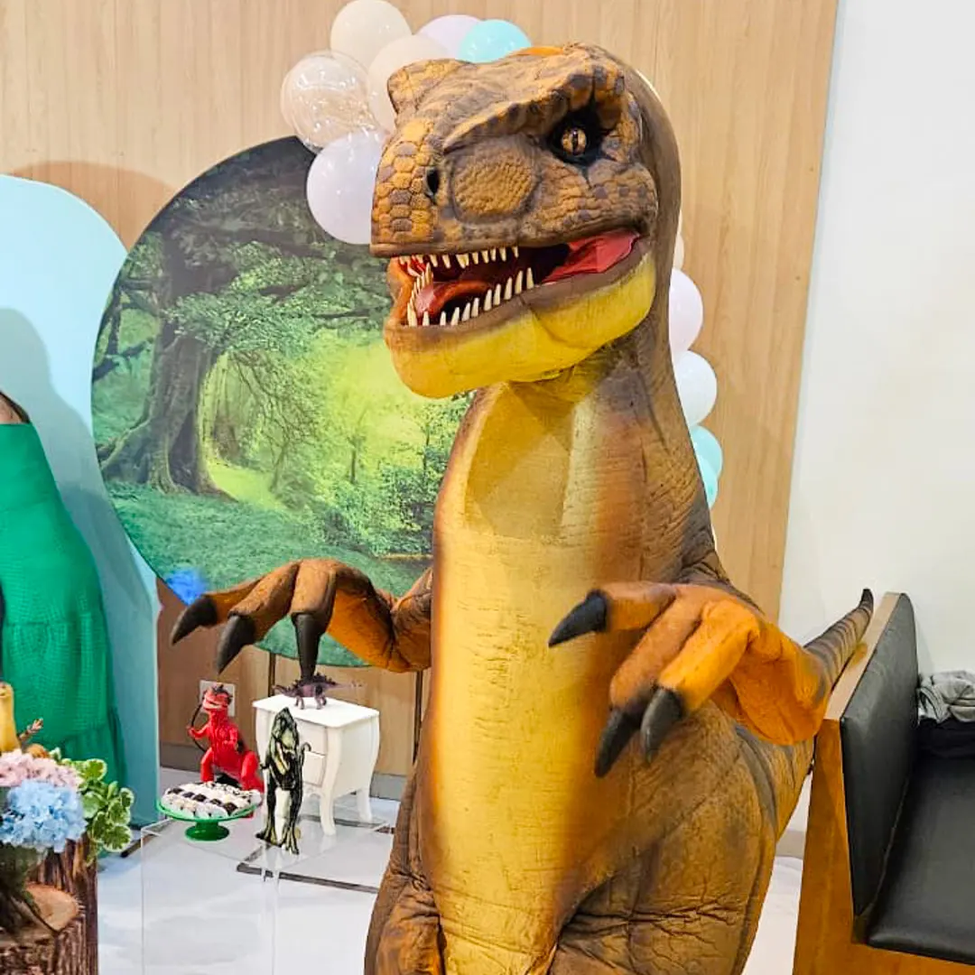 Gigantesco T-Rex Laranja Personagem Vivo rugindo na entrada triunfal da festa infantil