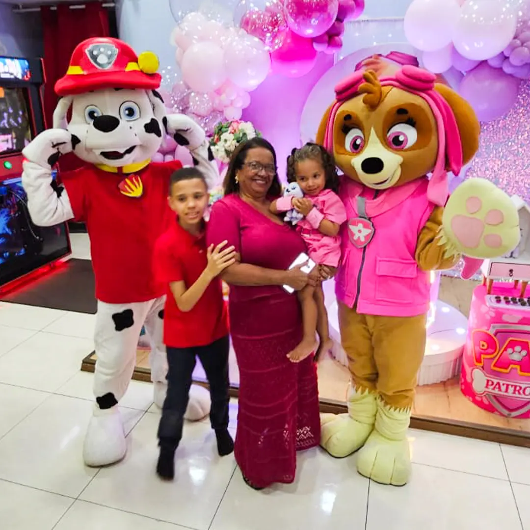 Personagem vivo posando com família em frente a um painel decorativo bem iluminado em salão de festas.